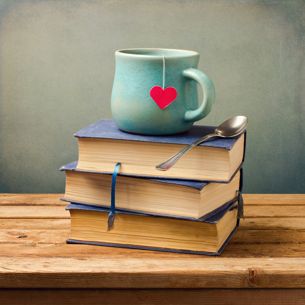 Old vintage books and a cup with a paper heart on a wooden table.