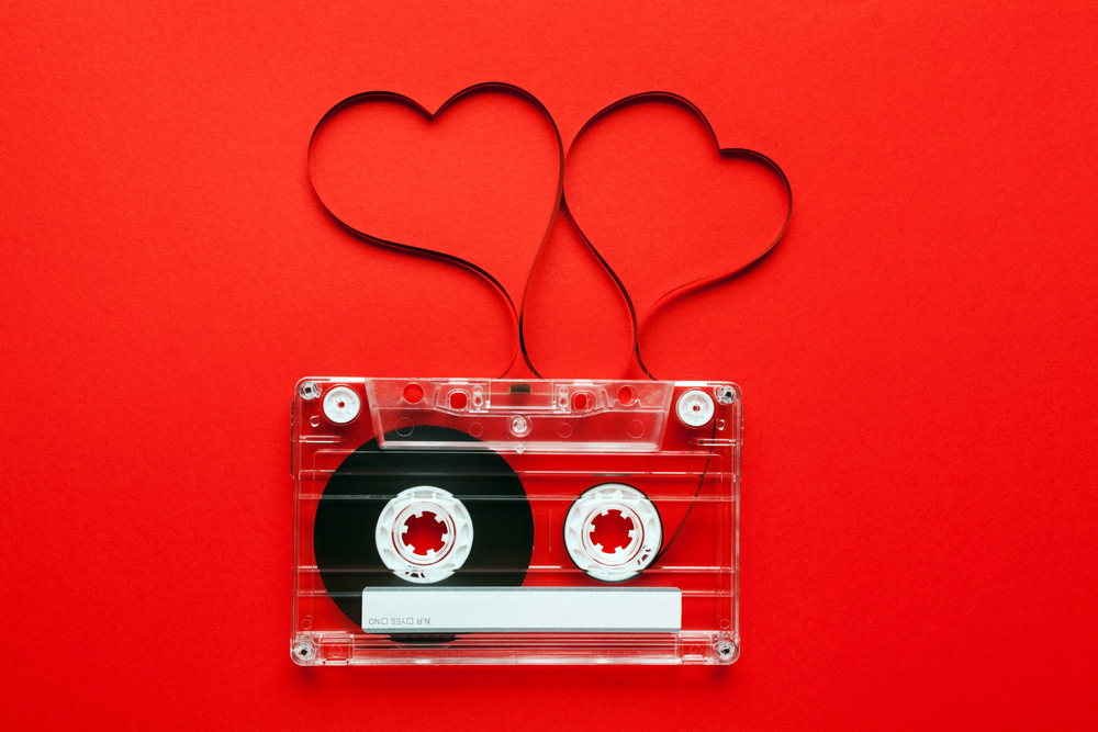 Vintage audio cassette with loose tape shaping two hearts on red background.